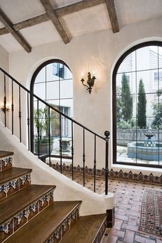 a staircase leading up to two large windows in a home with tiled flooring and wooden handrails