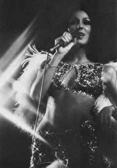 a black and white photo of a woman in a disco outfit singing into a microphone