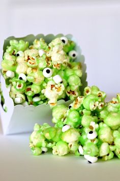 green popcorn with googly eyes on it sitting next to a white box filled with candy