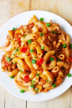 a white plate topped with pasta covered in sauce and green onions on top of a wooden table