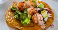 a taco with shrimp, lettuce and tomato on it sitting on a plate