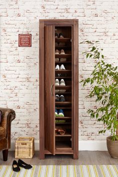 a wooden shoe cabinet sitting in front of a brick wall next to a chair and potted plant