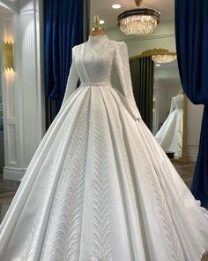 a white wedding dress on display in front of a mirror with blue curtains and chandelier