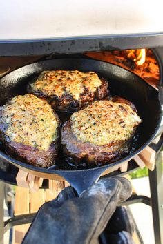 three hamburger patties cooking in a cast iron skillet over an open fire pit