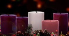 three lit candles surrounded by holly and pine cones