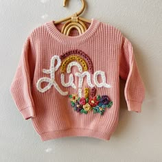 a pink sweater hanging on a wall with the word love spelled in white letters and flowers