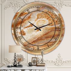 a large clock on the wall above a white table with a lamp and two pictures