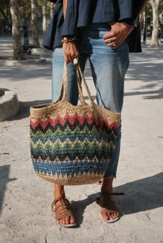 a woman is holding a multicolored bag on her feet while standing in the street