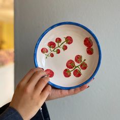 a person holding a bowl with strawberries painted on the side and flowers drawn on it