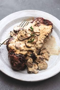 a white plate topped with steak covered in mushrooms and gravy next to a fork