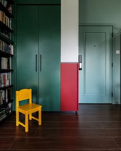 a yellow chair sitting in front of a book shelf next to a green cabinet and bookshelf