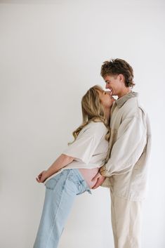 a man and woman standing next to each other in front of a white wall kissing