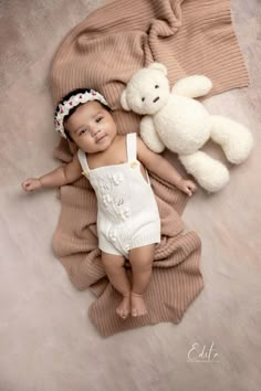 a baby laying on top of a blanket next to a teddy bear