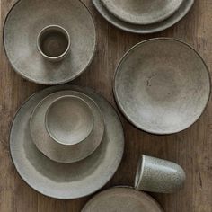 a wooden table topped with lots of gray plates and cups on top of it's sides