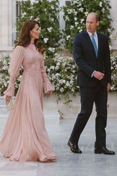 the duke and princess are walking together in front of some white flowered bushes, one is wearing a pink dress