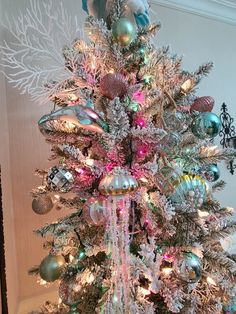 a white christmas tree with pink, green and blue ornaments on it's branches