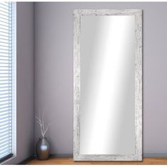 a large white framed mirror sitting on top of a wooden floor next to a window