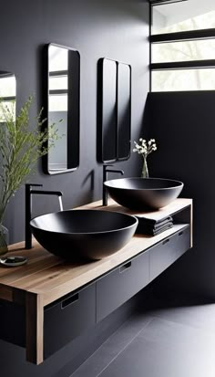 two black bowls sit on a wooden counter in front of mirrors and vase with flowers