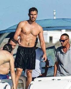 a shirtless man standing on top of a boat next to another man in shorts