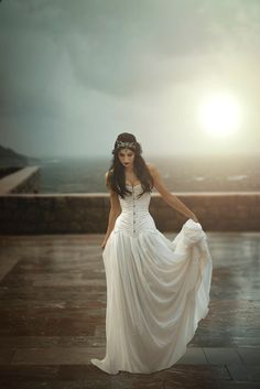 a woman in a white dress is posing for a photo with the sun behind her