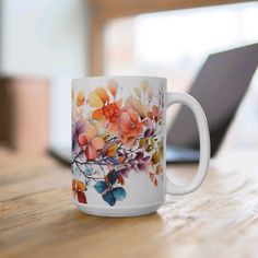 a white coffee mug sitting on top of a wooden table next to a laptop computer