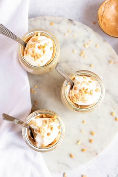 three jars filled with desserts on top of a white table next to spoons