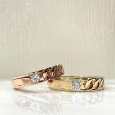 two gold wedding bands with diamonds on them sitting next to each other in front of a white background