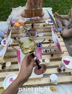 a person holding a wine glass in front of a table full of paintbrushes