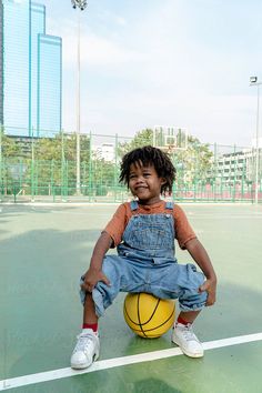 a young child sitting on top of a tennis court holding a yellow ball