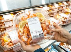 a person holding up a package of food in front of some trays filled with food