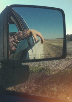 a person's reflection in the side view mirror of a car on a dirt road