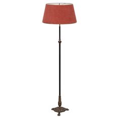 a floor lamp with a red shade on the base and a black metal pole underneath it