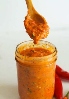 a spoon full of sauce being lifted from a jar with chili peppers in the background