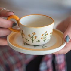 a woman holding a cup and saucer with yellow flowers on the rim, in her hands