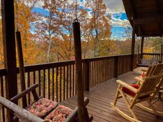 two rocking chairs on the front porch of a cabin with autumn foliage in the background