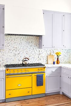 a yellow stove top oven sitting inside of a kitchen next to white cabinets and wooden floors