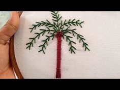 someone is stitching a palm tree on a piece of white fabric with red thread