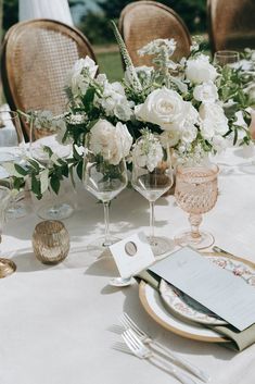 the table is set with white flowers and place settings