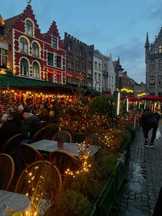 people are sitting at tables in the middle of an open air market with christmas lights on them