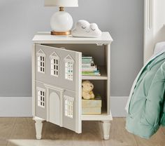 a small white doll house on a nightstand next to a bed