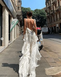 a woman is walking down the street with her back to the camera and wearing a white dress