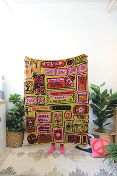 a large yellow blanket with pink and green designs on it sitting next to potted plants