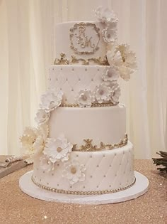 a three tiered wedding cake with white flowers on the top and gold trimmings