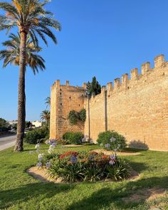 an old brick castle with palm trees and flowers in the foreground