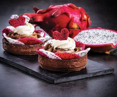 two desserts with whipped cream and dragon fruit on the side, sitting on a slate platter