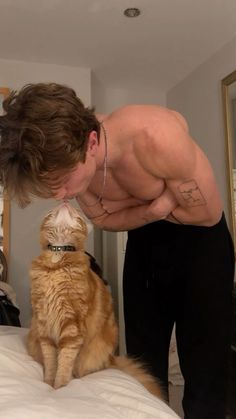 a man with his arm around an orange cat that is sitting on top of a bed