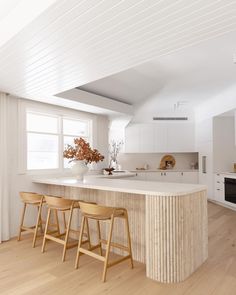 a kitchen with white cabinets and wooden stools next to an island in the middle