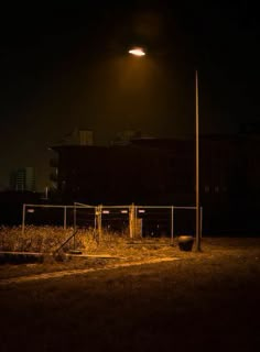 an empty field at night with a street light in the distance and buildings in the background