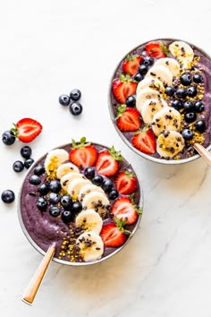 two bowls filled with blueberries, strawberries and bananas on top of a white table