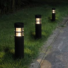 three black and gold outdoor lights on the side of a road next to some grass